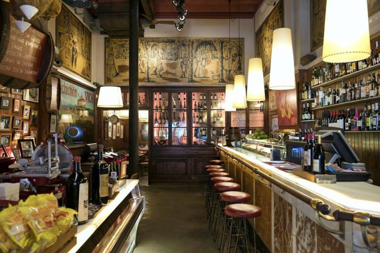 Local histórico Nos llaman un clásico de toda la vida, pero nosotros preferimos llamarlo la casa de todos nuestros clientes y clientas y de sus hijos e hijas. Casa Alfonso Inicios Fue en el año 1934 cuando se inauguró Casa Alfonso. Los protagonistas de ese evento fueron el bisabuelo Alfonso junto la bisabuela Rosario, la 1a generación de la familia, los que dirigieron el establecimiento. Además, el local abrió sus puertas con lo que hasta el momento funcionaba como un almacén de curtidos en una época dura, nada fácil para Barcelona, debido a que 2 años después empezó una Guerra Civil en España que duró 3 años ,desde 1936 hasta el fin de la contienda en el 1939.  Desde que Casa Alfonso abrió sus puertas, se conocía como la emblemática charcutería-colmado donde ir a comprar los mejores ibéricos y mariscos, pudiendo degustar allí mismo sus productos, deleitándose también con algún que otro bocadillo preparado con pan vienés, o con el famoso Llonguet , por nuestra ya conocida Abuela Ramona y Abuelo Alfonso, siempre tan atentos con el público, dando lo mejor de ellos. Pero llegados los 70, gracias a un cliente de la Casa, curioso por probar otros tipos de pan, se incorporó por primera vez en Barcelona el hoy típico bocadillo en pan de barra flauta ,muy similar a la clásica baguette francesa . Llegados los años 80 tocó compartir conocimiento y ceder parte de la dirección a la tercera generación de Alfonsos, el actual propietario. Quien adaptó Casa Alfonso a lo que hoy conocemos como Taberna histórica y Colmado Gourmet Alfonso, con una selecta bodega, platos, tapas, selección de ibéricos y repostería , dejando de ser el hasta entonces bar de bocadillos de referencia de Barcelona para convertirse en la imprescindible referencia gastronómica, siempre manteniendo la tradición y esencia en su mobiliario y platos, elaborados con el mismo mimo, amor y detalle de entonces, tal como los preparaban las abuelas de la casa. En la actualidad, Casa Alfonso sigue siendo la Taberna Histórica y Colmado Gourmet que ofrece su propia marca de ibéricos y su amplia selección de productos 100% ecológicos, además de dar paso a la cuarta generación, una generación encabezada por Claudia, ofreciendo su detalle, mimo y exigencia, de la misma manera que lo han hecho todas las mujeres de la familia..